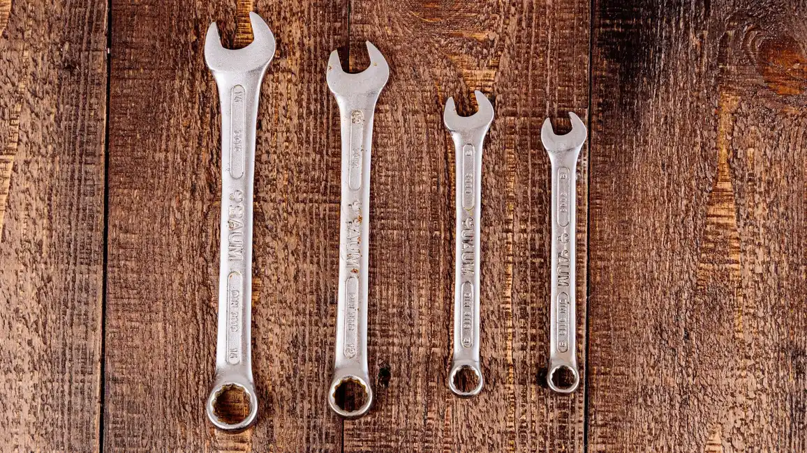 A set of metal wrenches laid out on a wooden workbench